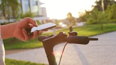 Scooter 'a bağlanan cep telefonunun ayrıntıları. Elektronik Scooter 'la Cep Telefonu Bağlayan Adam' ın yakın çekimi, Yavaş Hareket. Electric Scooter, Modern Şehir Ulaşım, Yeni Teknoloji.