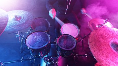Drummer Playing on Drums Assembly. Dramatic Scene with Colored Neon Lights. Concert and Performance Theme. clipart