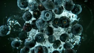 Düşen yaban mersinlerinin süper yavaş bir şekilde siyah arka planda suya düşmesi. Yüksek hızlı sinema kamerası, 1000 fps..