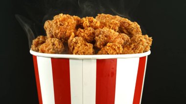 Kağıt kovada kızarmış tavuk parçaları, siyah arka planda izole edilmiş. Hurda Gıda Konsepti.