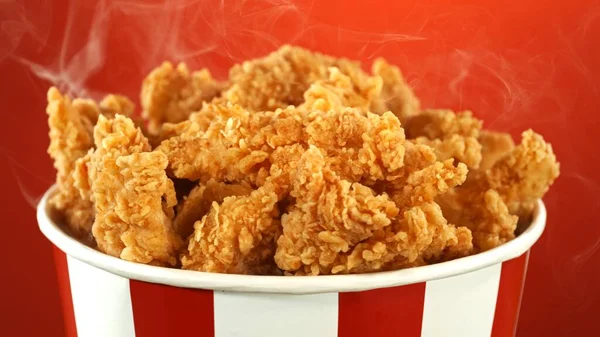 Fried Chicken Pieces in Paper Bucket, Isolated on Colored Background. Concept of Junk Food.