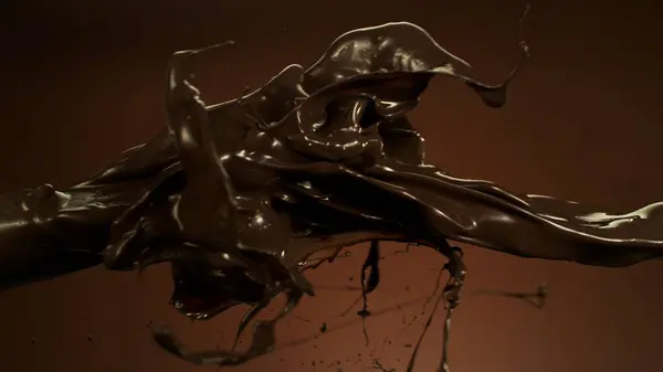 Geschmolzene Schokolade Spritzt Die Luft Isoliert Auf Braunem Hintergrund lizenzfreie Stockfotos