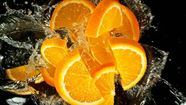 Freeze Motion of Flying Orange Slices into Water, Black Background. Concept of Flying Fresh Fruit, Splashing into Water.