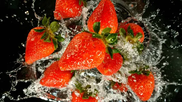 Freeze Motion of Flying Strawberries into Water, Black Background. Concept of Flying Fresh Fruit, Splashing into Water.