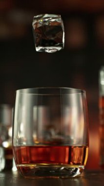 Bir bardak viskiye düşen buzun süper yavaş hareketi. High Speed Cinema Camera 'da çekildi, 1000 fps. Kamera hareket halinde. Arkaplanda Bar, Odak Derinliği Düşük. Dikey Görünüm Oranı.