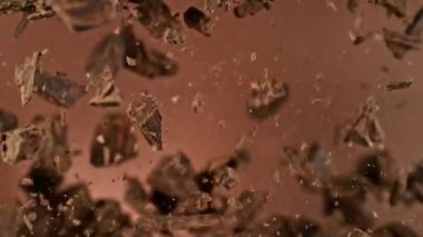 Havada Uçan Çikolata Parçalarının Süper Yavaş Hareketi. Kahverengi Arka plan 'da izole edilmiş. Kamera Hareket Ediyor. High Speed Cinema Camera 'da çekildi, 1000 fps. Hız Rampası Efekti.