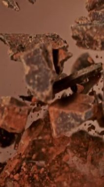 Havada Uçan Çikolata Parçalarının Süper Yavaş Hareketi. Kahverengi Arka plan 'da izole edilmiş. Kamera Hareket Ediyor. High Speed Cinema Camera 'da çekildi, 1000 fps. Dikey Görünüm Oranı.