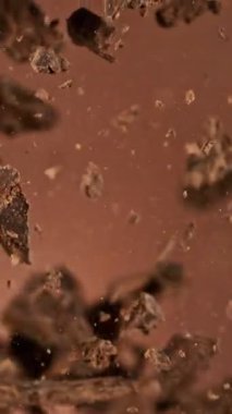 Havada Uçan Çikolata Parçalarının Süper Yavaş Hareketi. Kahverengi Arka plan 'da izole edilmiş. Kamera Hareket Ediyor. High Speed Cinema Camera 'da çekildi, 1000 fps. Dikey Görünüm Oranı.