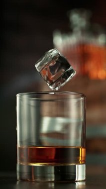 Bir bardak viskiye düşen buzun süper yavaş hareketi. High Speed Cinema Camera 'da çekildi, 1000 fps. Kamera hareket halinde. Arkaplanda Bar, Odak Derinliği Düşük. Dikey Görünüm Oranı.
