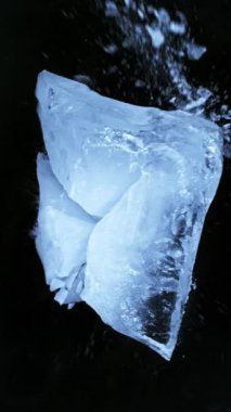 Siyah zemin üzerine düşen buz parçasının süper yavaş çekimi. Yüksek hızlı sinema kamerası, 1000 fps. Dikey görünüm oranı.