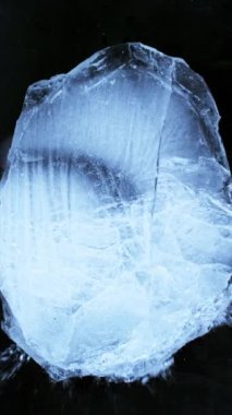 Siyah zemin üzerine düşen buz parçasının süper yavaş çekimi. Yüksek hızlı sinema kamerası, 1000 fps. Dikey görünüm oranı.