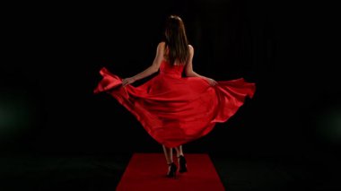 Yakut kırmızısı elbiseli, çarpıcı siyah saçlı kadın ve yüksek topuklu ayakkabı giyen zarif siyah arka plan pozu, dramatik ve zarif bir moda efekti için süper yavaş çekimde yakalandı..