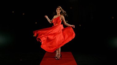Uçan kumaşla dans eden kırmızı elbiseli kadın, el sallayan kumaşla poz veren moda mankeni kız. Siyah arkaplanda izole.