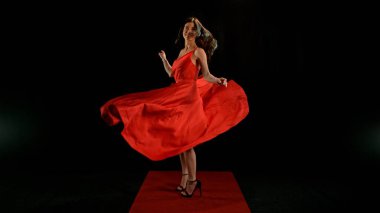Uçan kumaşla dans eden kırmızı elbiseli kadın, el sallayan kumaşla poz veren moda mankeni kız. Siyah arkaplanda izole.