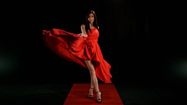 Uçan kumaşla dans eden kırmızı elbiseli kadın, el sallayan kumaşla poz veren moda mankeni kız. Siyah arkaplanda izole.