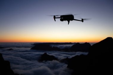 Drone Silhouette Sunset Light 'ta. Arka planda Yüksek Dağlar ve Vadide Bulutlar. Açık gökyüzü, Düşük Işık, Seçici Odak.