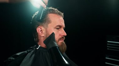 Berber dükkanındaki sakallı genç adam. Berber saç kesimini hazırlıyor. Karanlık Atmosfer, Kara Arkaplan. Berber ve Müşteri kavramı.