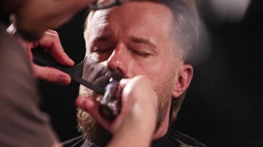 Berber dükkanındaki sakallı genç adam. Berber saç kesimini hazırlıyor. Karanlık Atmosfer, Kara Arkaplan. Berber ve Müşteri kavramı.