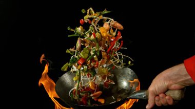 Şef 'in tavadan çıkan et karışımıyla birlikte Asya sebzelerini ateşe atmasına yakın çekim. Siyah arka planda taze Asya yemeği hazırlama.