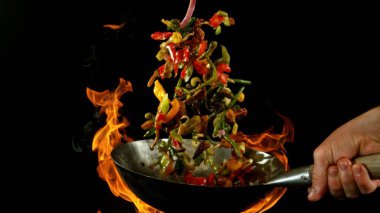 Şef 'in tavadan çıkan et karışımıyla birlikte Asya sebzelerini ateşe atmasına yakın çekim. Siyah arka planda taze Asya yemeği hazırlama.