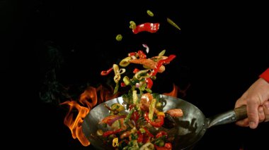 Şef 'in tavadan çıkan et karışımıyla birlikte Asya sebzelerini ateşe atmasına yakın çekim. Siyah arka planda taze Asya yemeği hazırlama.