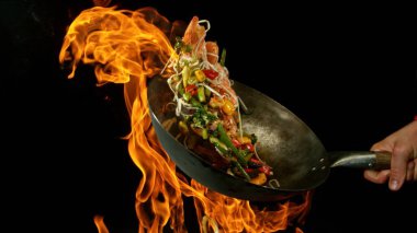 Şef 'in tavadan çıkan et karışımıyla birlikte Asya sebzelerini ateşe atmasına yakın çekim. Siyah arka planda taze Asya yemeği hazırlama.