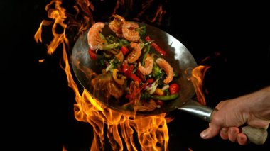 Şef 'in tavadan çıkan et karışımıyla birlikte Asya sebzelerini ateşe atmasına yakın çekim. Siyah arka planda taze Asya yemeği hazırlama.