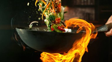 Wok Pan 'ın Dondurucu Hareketi ve Havadaki Uçan Malzemeler ve Ateş Alevleri. Arka planda Mutfak İçi.