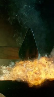 Demircinin sinematik yakın çekimi örsün üzerinde kıvılcımlar uçuşurken kızgın demir dövmesi. Karanlık arka planda dramatik ışıklandırma ile yüksek hızlı kamera ile 300 fp 'de çekildi. Dikey görünüm oranı.