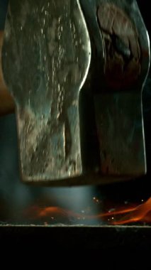 Demircinin sinematik yakın çekimi örsün üzerinde kıvılcımlar uçuşurken kızgın demir dövmesi. Karanlık arka planda dramatik ışıklandırma ile yüksek hızlı kamera ile 300 fp 'de çekildi. Dikey görünüm oranı.