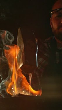 Demircinin sinematik yakın çekimi örsün üzerinde kıvılcımlar uçuşurken kızgın demir dövmesi. Karanlık arka planda dramatik ışıklandırma ile yüksek hızlı kamera ile 300 fp 'de çekildi. Dikey görünüm oranı.