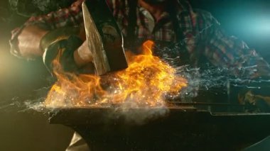 Demircinin sinematik yakın çekimi örsün üzerinde kıvılcımlar uçuşurken kızgın demir dövmesi. Karanlık arka planda dramatik ışıklandırma ile yüksek hızlı kamera ile 300 fp 'de çekildi. Kamera hareket halinde.