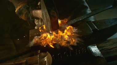 Demircinin sinematik yakın çekimi örsün üzerinde kıvılcımlar uçuşurken kızgın demir dövmesi. Koyu arkaplanda dramatik ışıklandırma ile yüksek hızlı kamera ile 1000 fps hızla çekilmiştir..