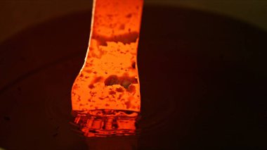 Işıldayan kızgın demirin soğuk suda söndürüldüğü yakın plan. Metal dövmesi ve soğutma kavramı.