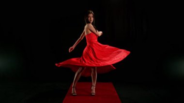 Yakut kırmızısı elbiseli çarpıcı siyah saçlı kadın ve yüksek topuklu zarif siyah arka plan pozu, Süper Yavaş Çekimde Yakalandı. Hız Rampası Efekti.