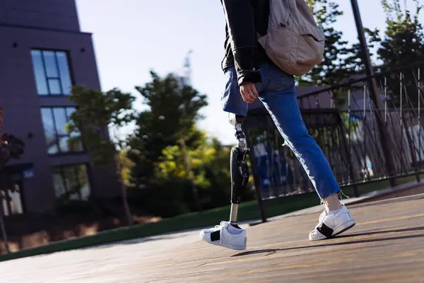 Close up of woman student with prosthetic leg walking in university campus. Woman with bionic leg. Woman with leg prosthesis equipment.