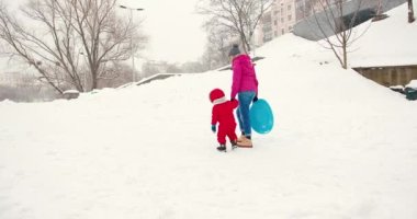 Anne ve küçük çocuk kışın karda eğleniyorlardı. Kış tatili eğlence kızak binme konsepti.