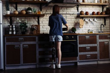 Protez bacaklı bir kadın yemek hazırlamak için tencereye esrar koyar. Modern mutfakta yeni tariflerle engelli deneyleri yapan genç bir kadın.