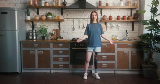 人工肢を持つブルネットの女性は 交差した腕を持つキッチンに立っています 障害のある女性は居心地の良いキッチンでカメラをポーズする自信を誇ります — ストック動画