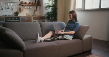 Özürlü bir kadın modern dizüstü bilgisayarla düşünce ve fikir beyan ediyor. Günlük kıyafetli bir kadın evdeki kanepede otururken internetten çalışıyor.