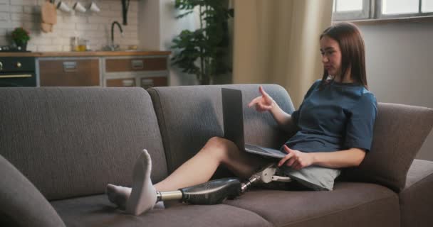 足の義足を持つ女性は ラップトップを介して同僚とやりとりします 障害のあるポジティブな女性は ビデオ通話を介して効果的にコミュニケーションするためにガジェットを使用します — ストック動画