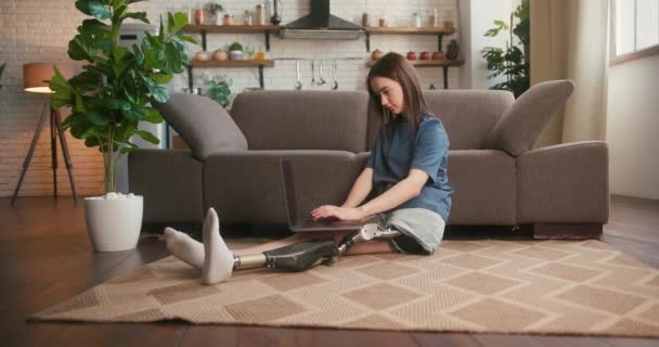 障害のある若いブルネット女性は スタートアッププロジェクトの計画をタイプするためにラップトップを使用しています タスクに完全に従事する女性は 現代のガジェットに取り組む床に座っています — ストック動画