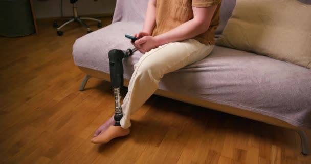 自宅でスマートフォンを使用して 膝移植足人工人工装置の上に義足障害を持つ男性アンプ 日常生活における切断障害者 — ストック動画