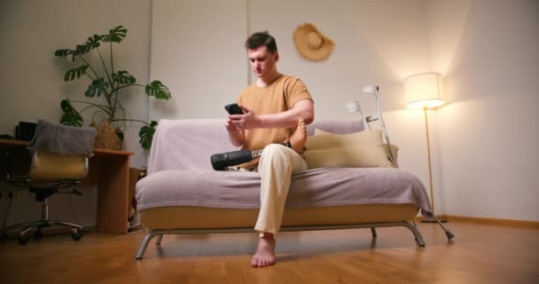 自宅でスマートフォンを使用して 膝移植足人工人工装置の上に義足障害を持つ男性アンプ 日常生活における切断障害者 — ストック動画