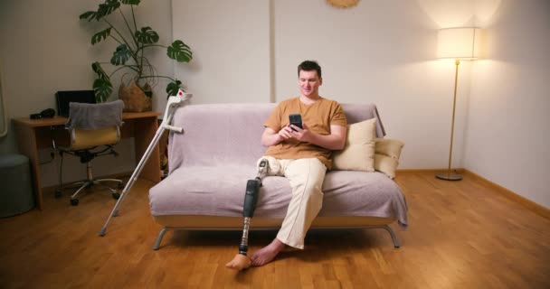 携帯電話でビデオ通話をするためにスマートフォンを使用して 上記の義足障害の義足人工デバイスを持つ男性アンプ 日常生活における切断障害者 — ストック動画