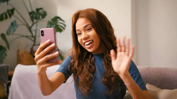 拉丁女人通过家里的智能手机视频通话 快乐的西班牙裔女士在网上会议上向朋友挥手致意 混合种族容忍 图库图片
