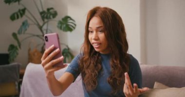 Latin kadın evdeki akıllı telefondan video ile konuşuyor. Çevrimiçi konferans sırasında neşeli İspanyol kadın el sallıyor. Karışık ırk toleransı