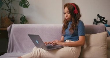 Laptop 'ta kulaklık takan Latin bir kadın evde çalışıyor. İspanyol serbest yazar kanepede oturan bilgisayarla ilgili makale yazıyor. Karışık ırk toleransı