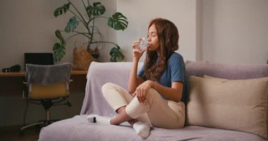 Kanepede oturan İspanyol kadın saf su içiyor. Rahat Latin Amerikalı kadın evinde temiz su ile ferahlatıyor. Karışık ırk toleransı