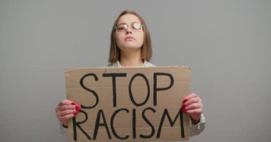 Kadın kartondan mesaj taşıyor. Irkçılığı ağır çekimde durdurun. Sarışın kız sistemik eşitsizlikleri ele almanın aciliyetini vurguluyor